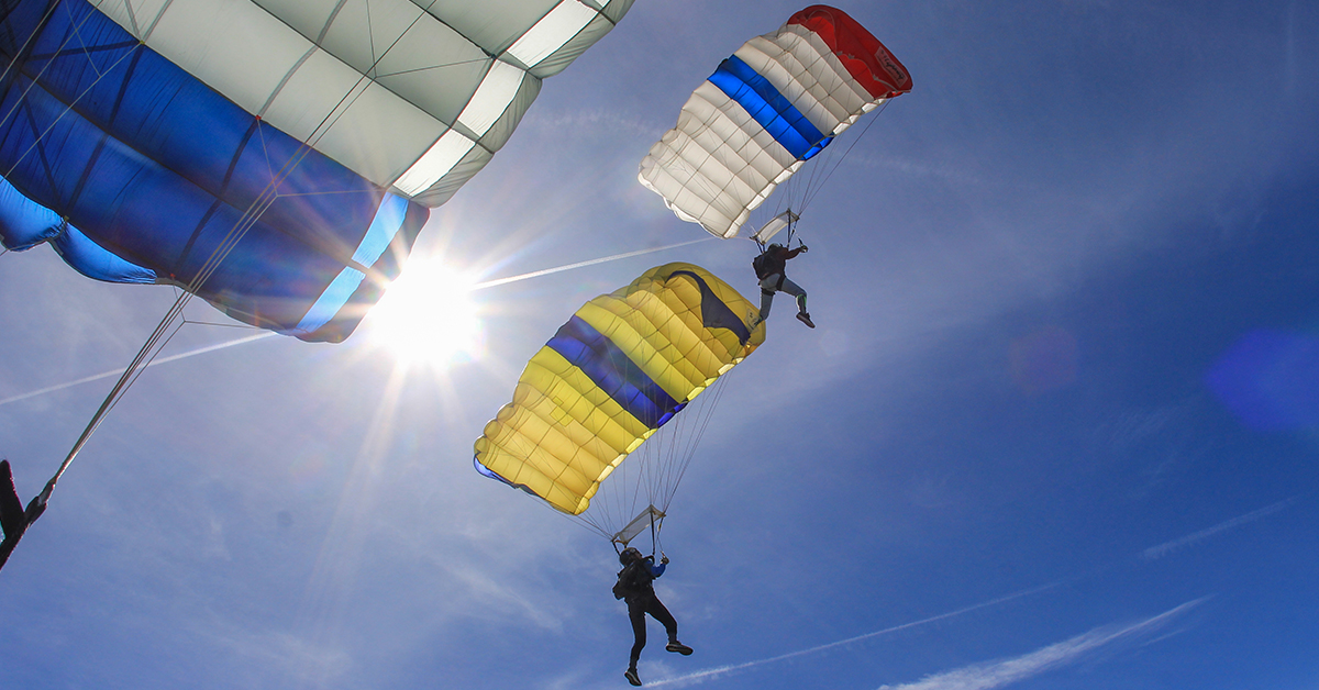 Skydivers, with colourful striped parachutes open, fall. Seen from below