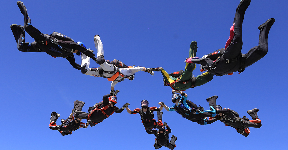 A group of skydivers hold hands in a circle as they fall.