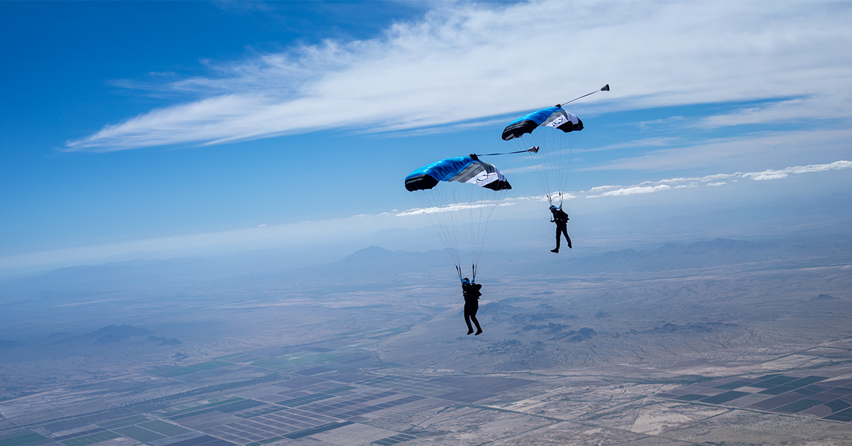 Skydivers coast through blue skies over patchwork fields