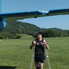 Adrian Ferguson poses on crutches next to the plane wing he became caught on.
