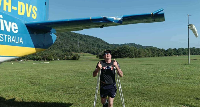 Adrian Ferguson poses on crutches next to the plane wing he became caught on.