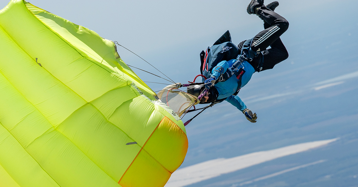A skydiver dressed in blue opens their bright yellow chute.